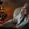 Elderly man quietly gazing at sparkling lights on small Christmas Tree.