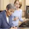 Senior woman fills medicine planner with help from a female caregiver.