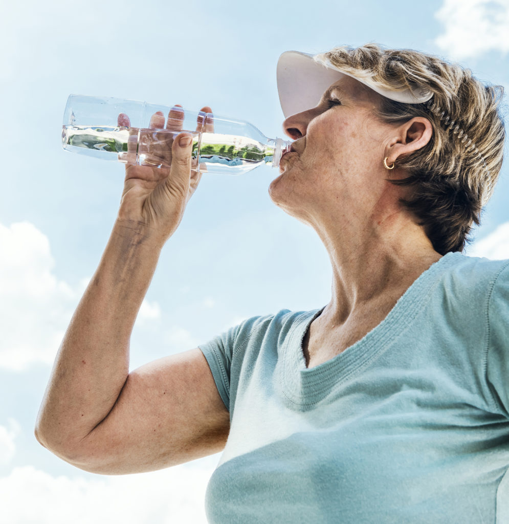 Older adult woman drinking water on a hot day after exercising.