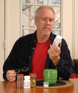 Senior man reading medication label at kitchen table.