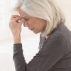 Senior woman in grey sweater holding her head with eyes closed in pain.