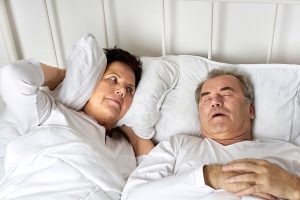 Senior couple in bed and wife covers ears due to snoring husband.