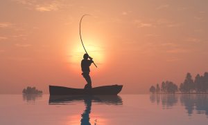 Silhouette of a fisherman in a boat. with a yellow sun and orange sky in background.
