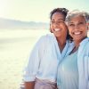 Asian mother and adult daughter smiling and hugging on a beach vacation.