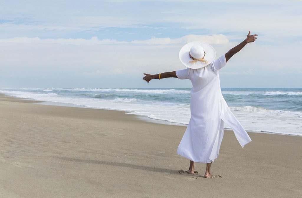 Happy African American woman on the beach with arms outstretched.