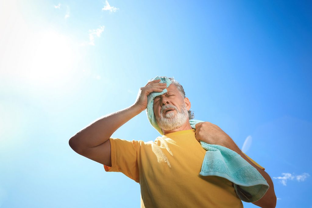 Senior man under hot summer sun and blue sky wipes his sweaty brow.