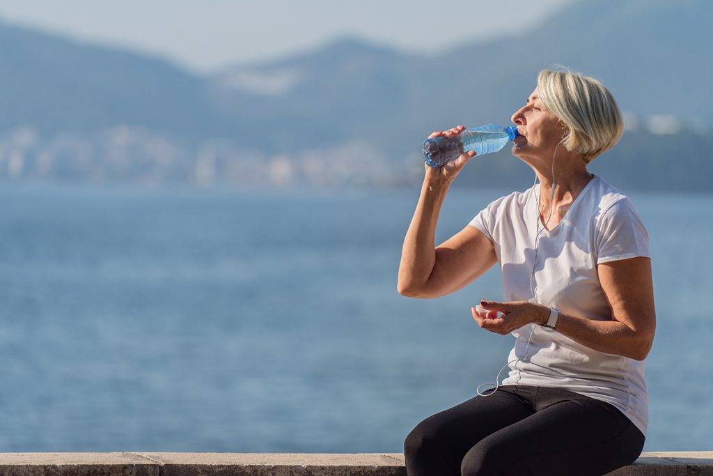 Attractive senior woman drinking from a cool bottle of water in summer sunshine.
