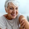 Pretty senior woman smiling and showing her arm with a bandaid where she got the flu vaccination.