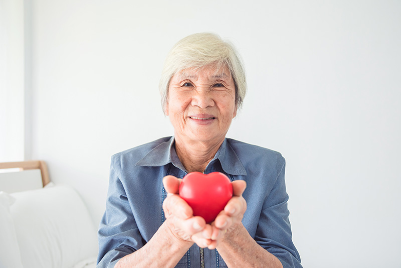 Smiling Asian woman holding a plastic heart shape.