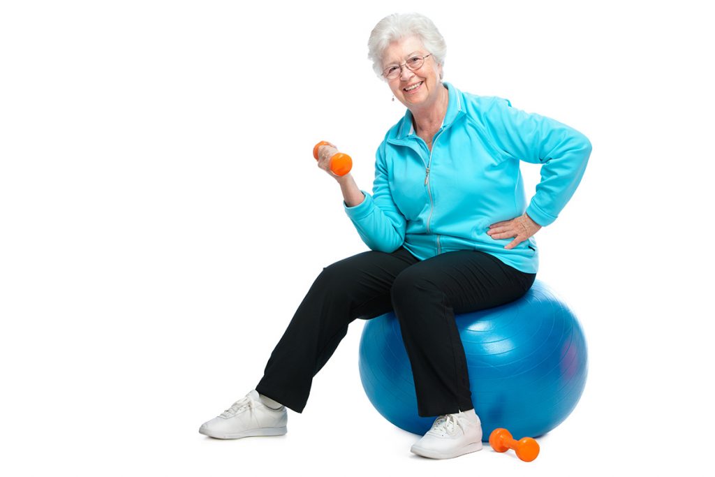 Senior woman smiling and sitting on an exercise ball using hand weights.